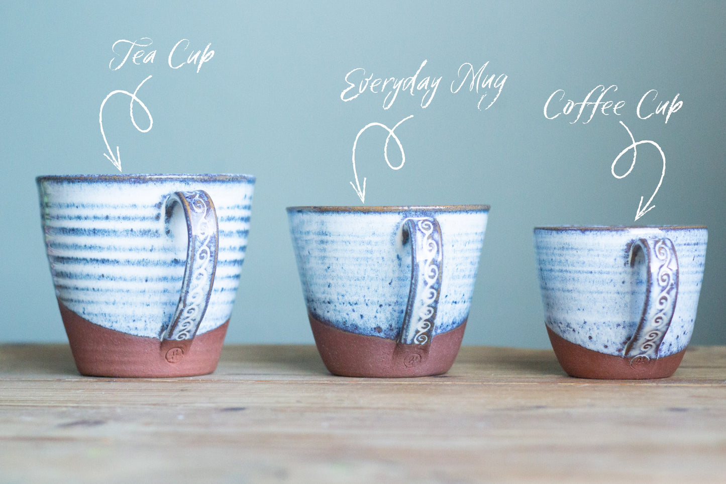 Three ceramic cups labeled 'Tea Cup', 'Everyday Mug', and 'Coffee Cup' on a wooden surface with a light blue background.