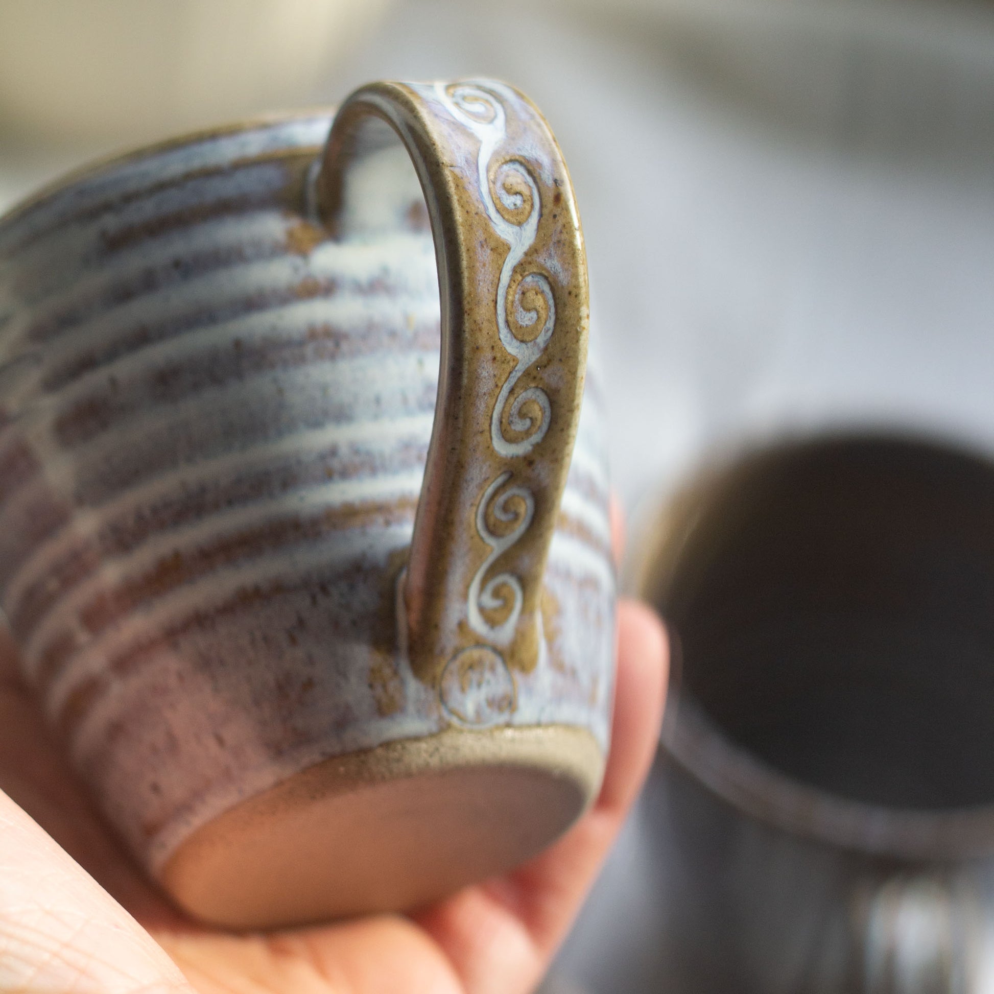 hand holding a ceramic coffee cup to show the decorative handle and flowing glaze