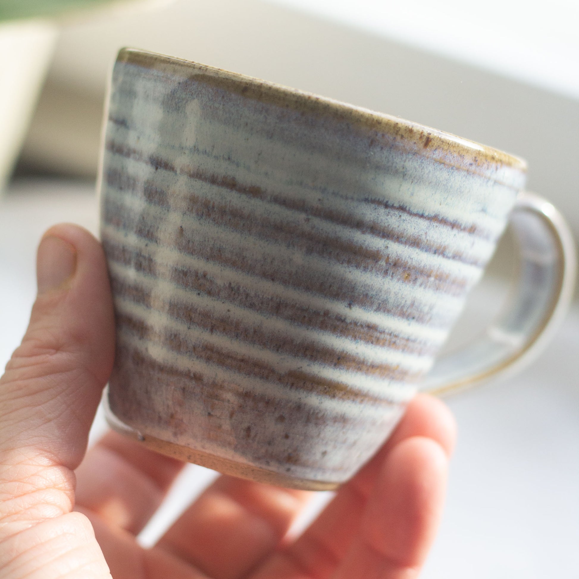 Hand holding a ceramic mug with visivable  hand throwing pattern