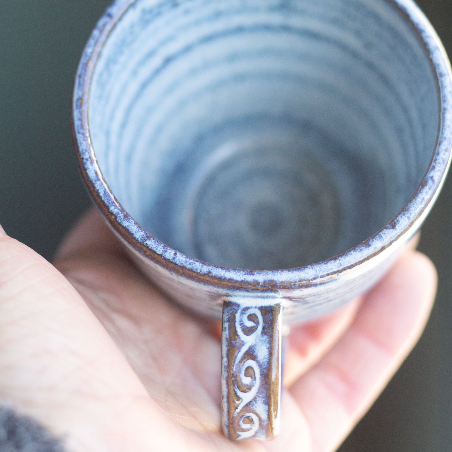 Hand holding a blue ceramic mug with a decorative handle.