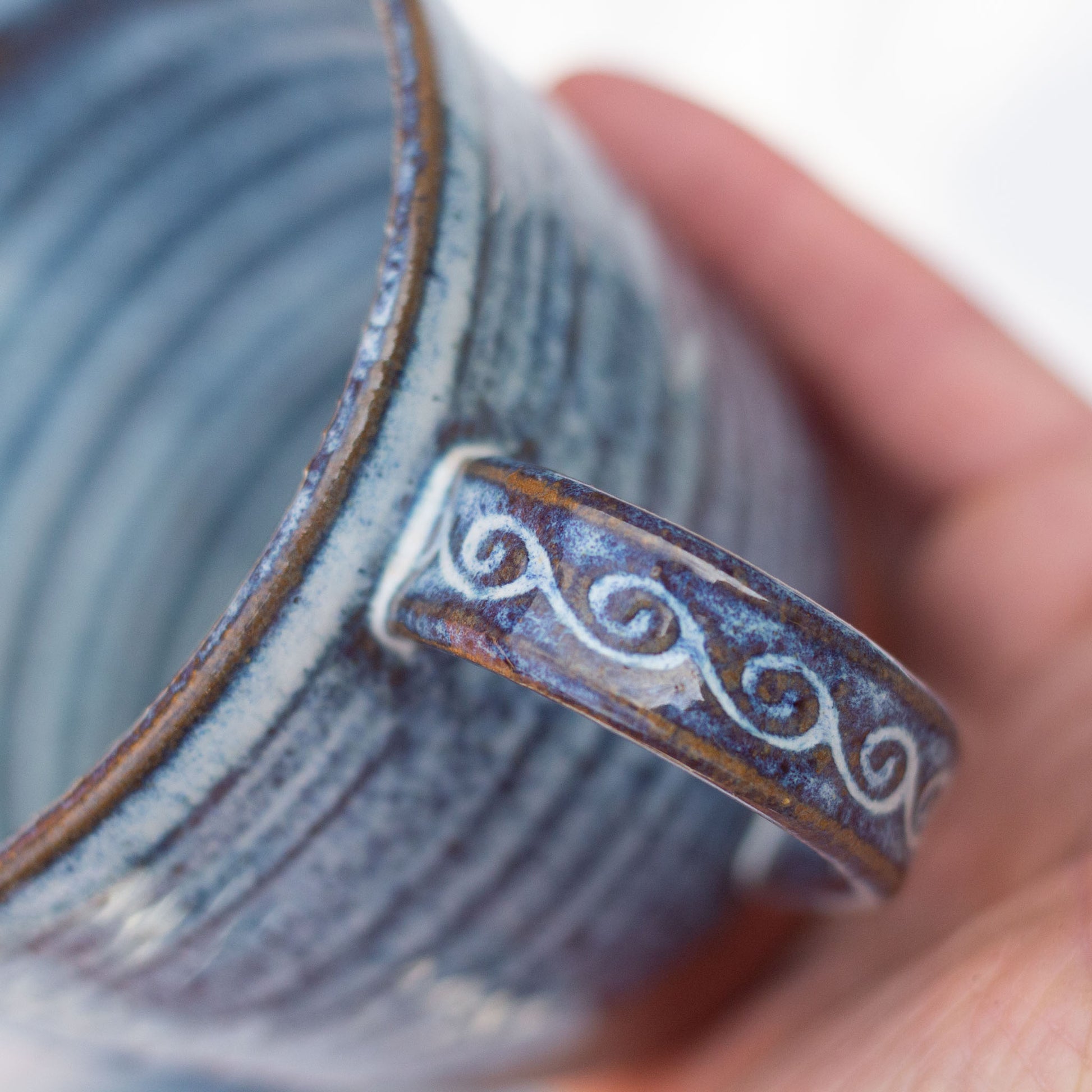 Ceramic mug with decorative handle held by a hand against a white background