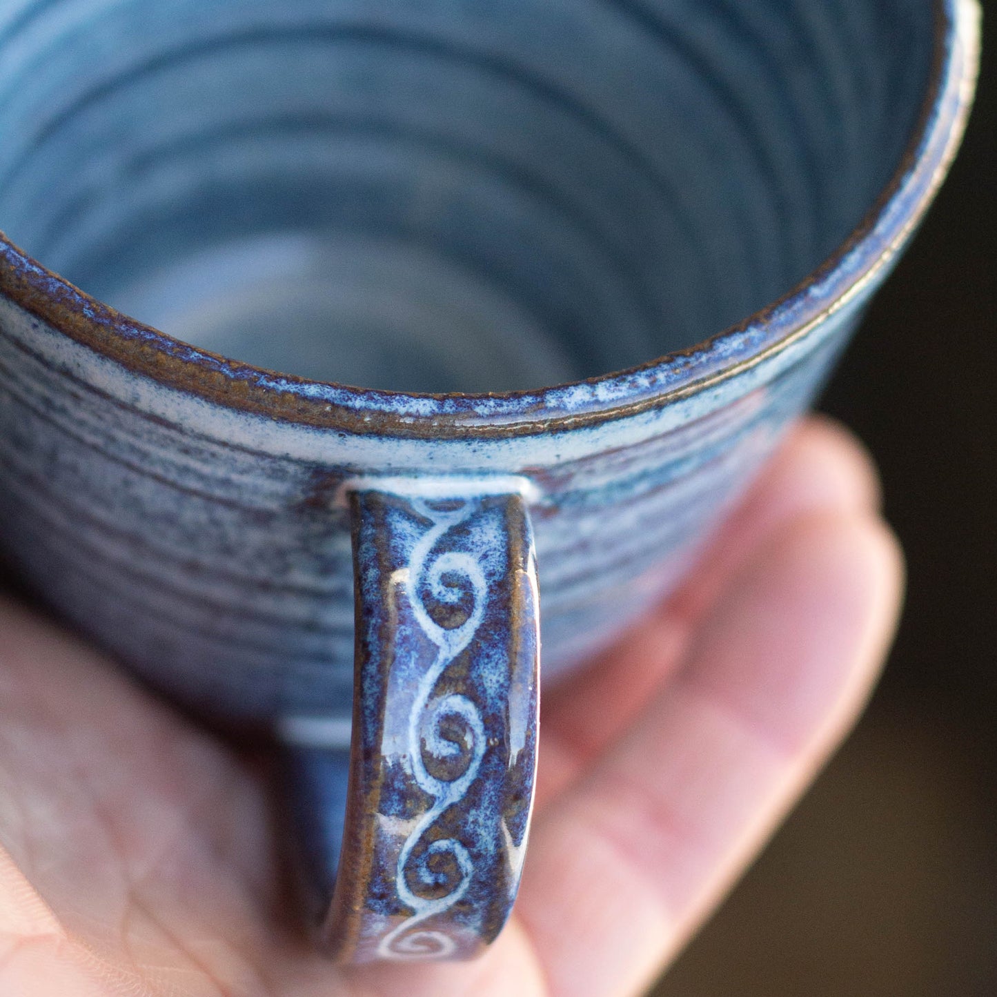 Hand holding a blue ceramic mug with swirling patterns on the handle