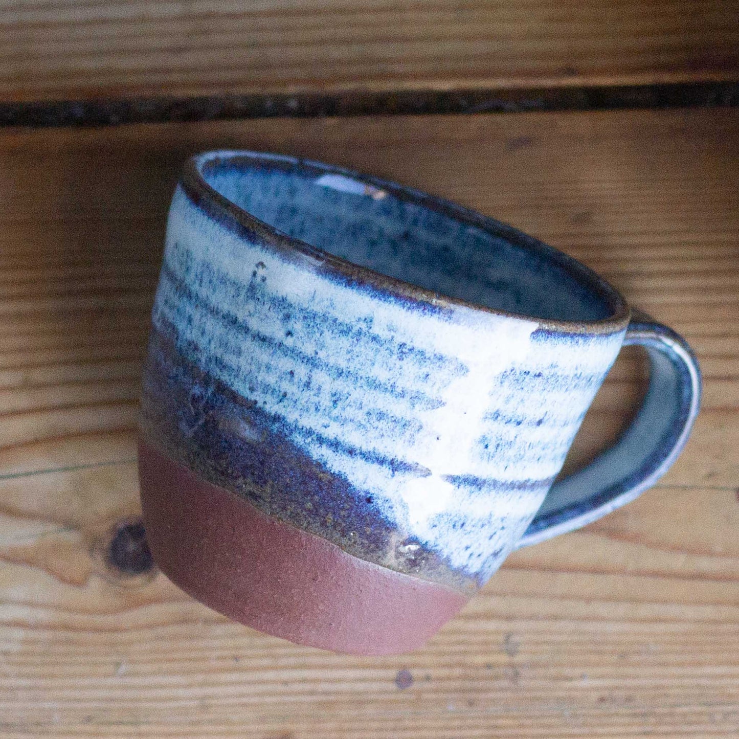 Ceramic coffee cup with blue and brown glaze on a wooden surface