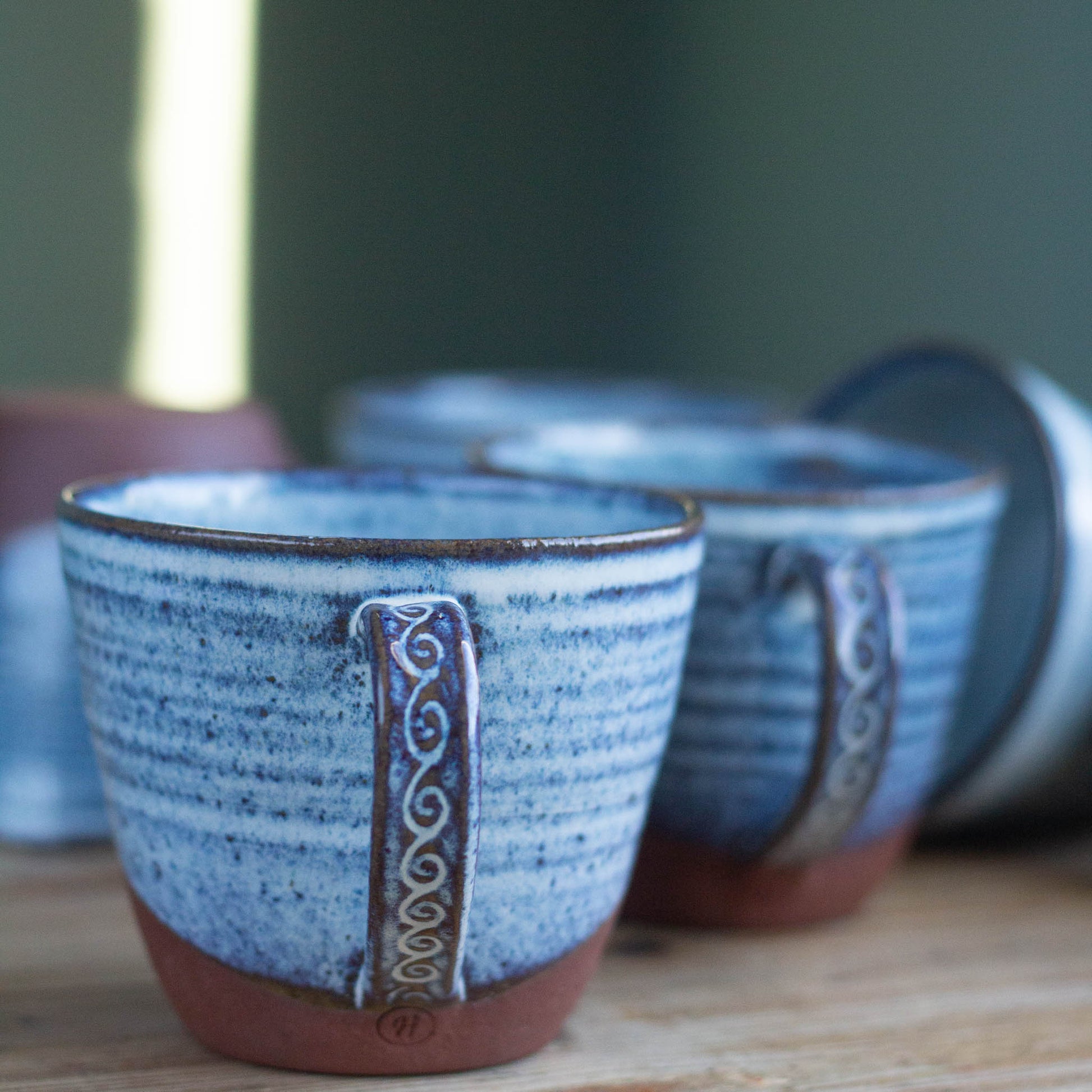 Handmade blue ceramic cup with red brown base and decorative handle on a wooden surface
