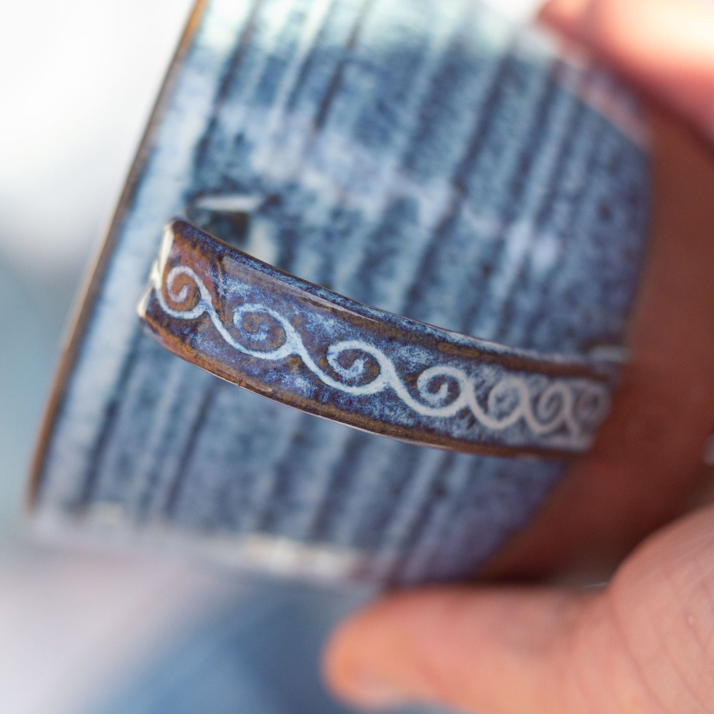 Close-up of a handmade blue ceramic cup with decorative patterns held by a hand.