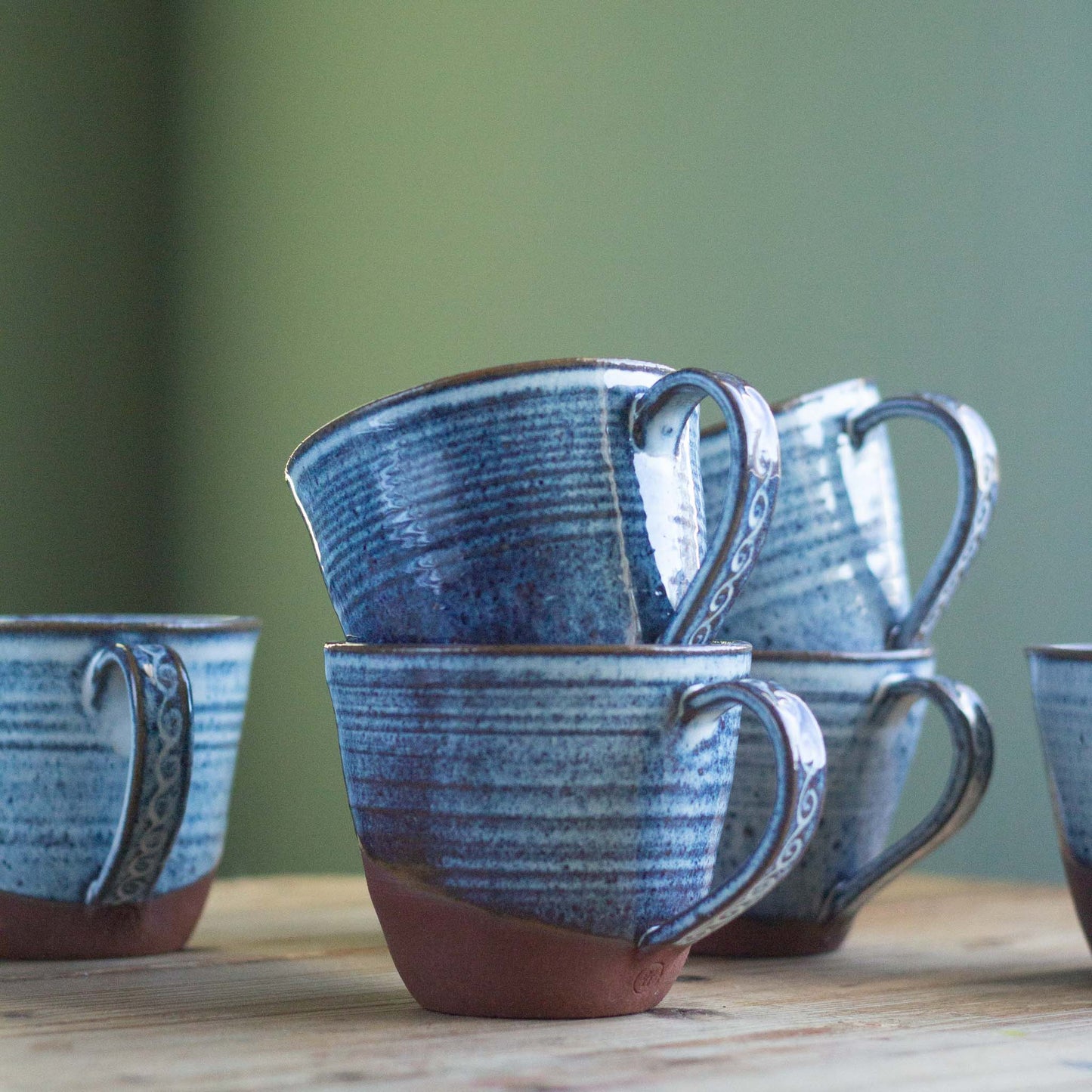 Set of blue ceramic mugs on a wooden surface with a green background