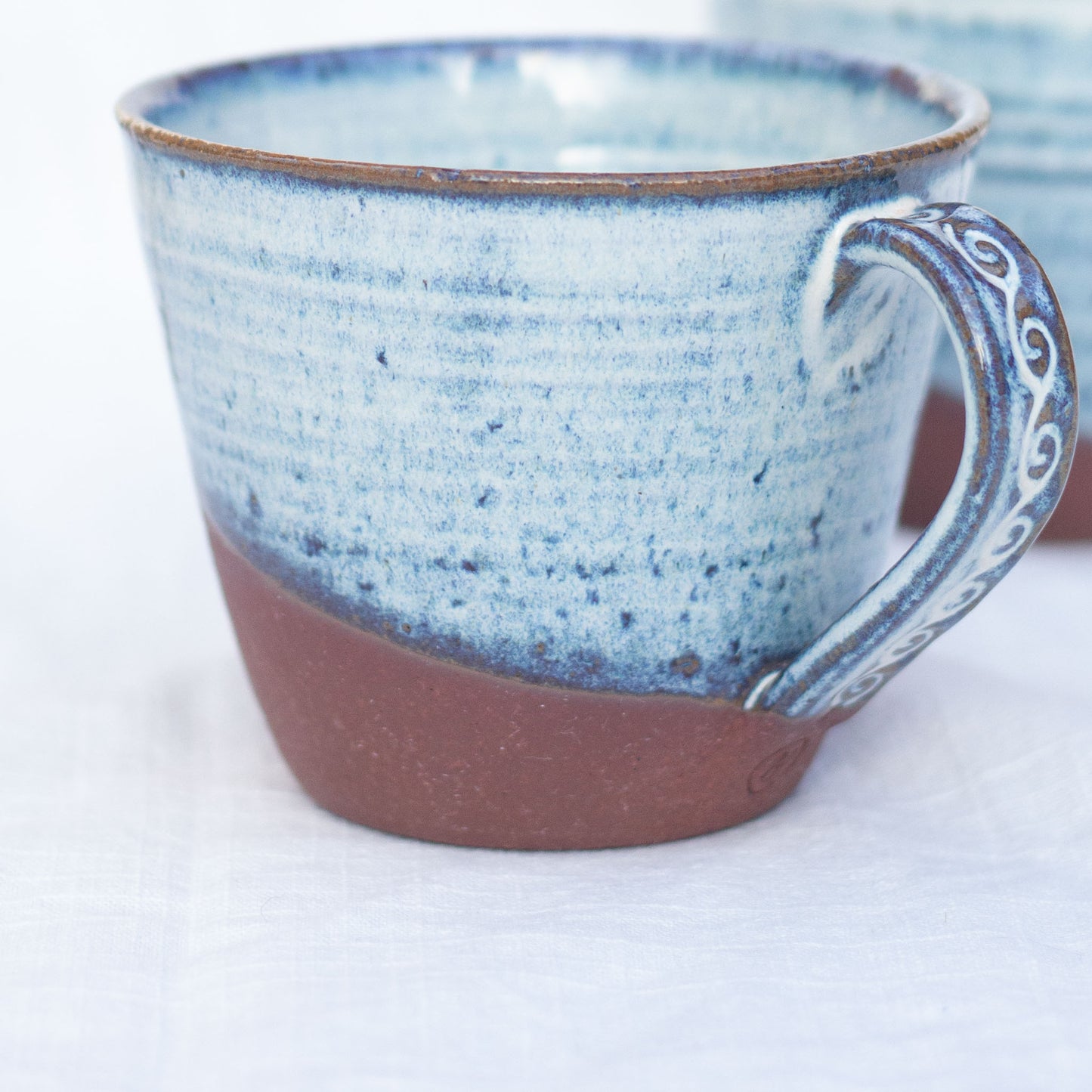 Ceramic mug with blue speckled glaze and red brown base on a white background