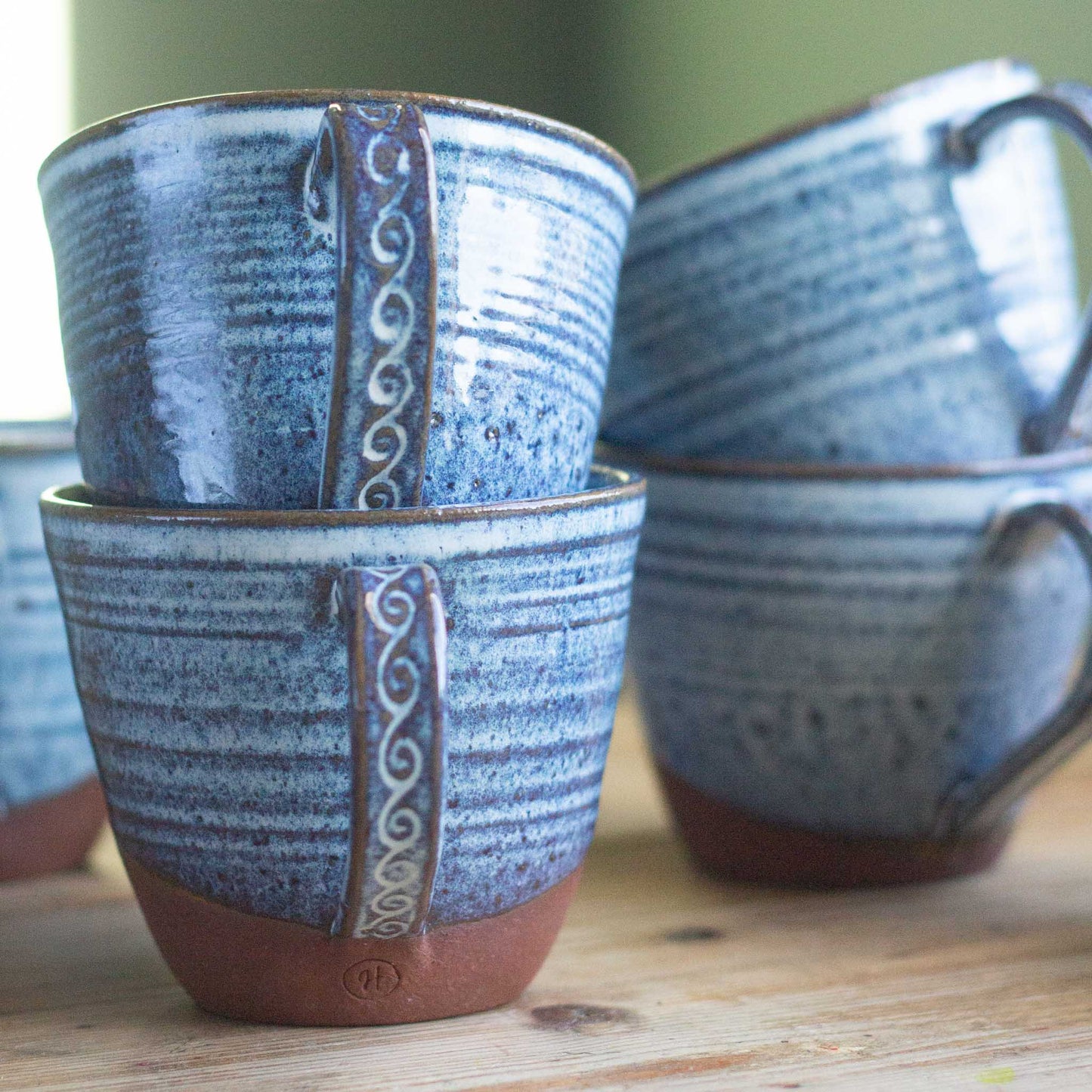 Set of blue handmade ceramic mugs with decorative handles on a wooden surface.