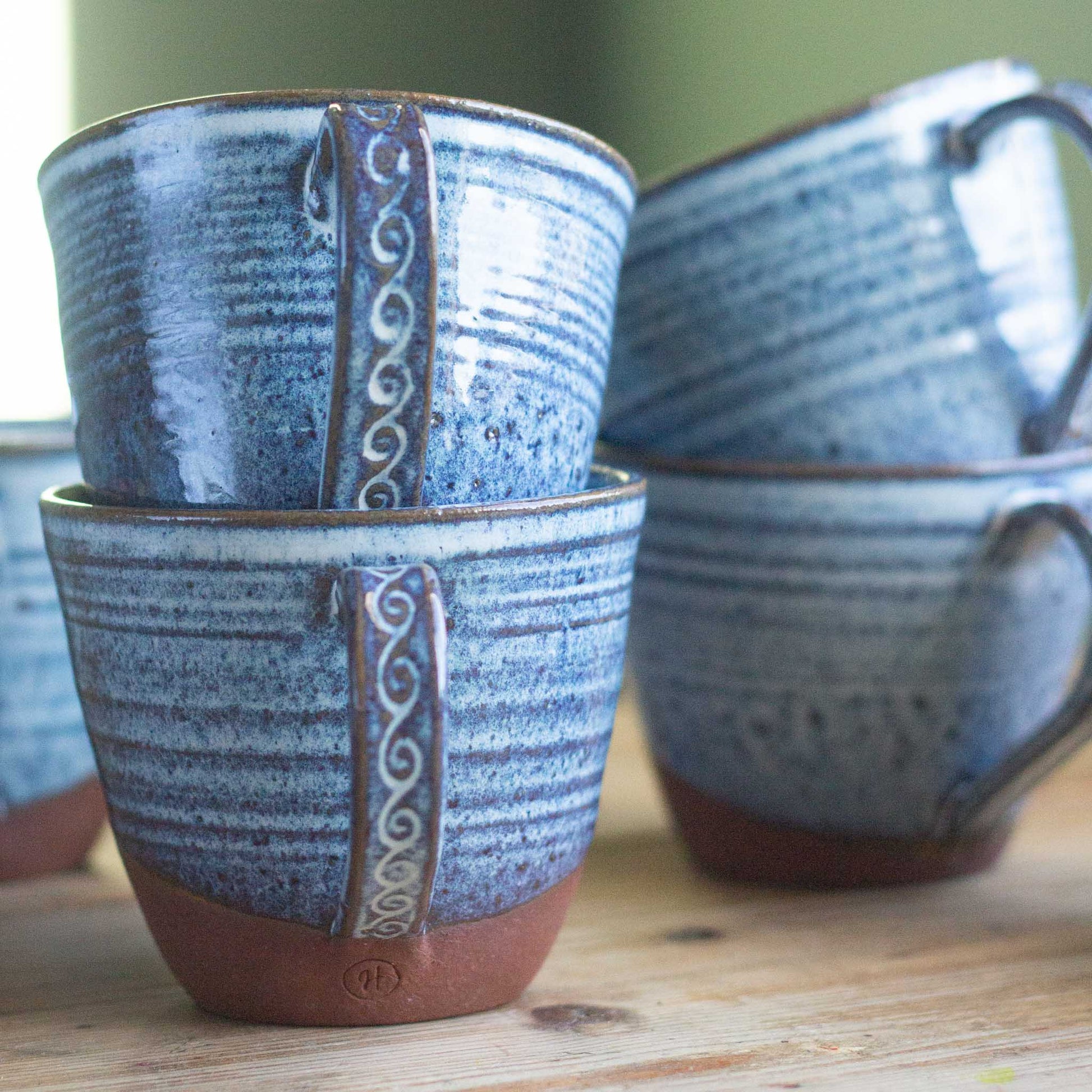 Set of blue handmade ceramic mugs with decorative handles on a wooden surface.
