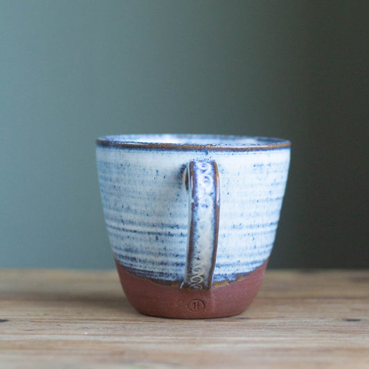 large handmade ceramic tea cup with white blue glaze and red clay on a wooden table