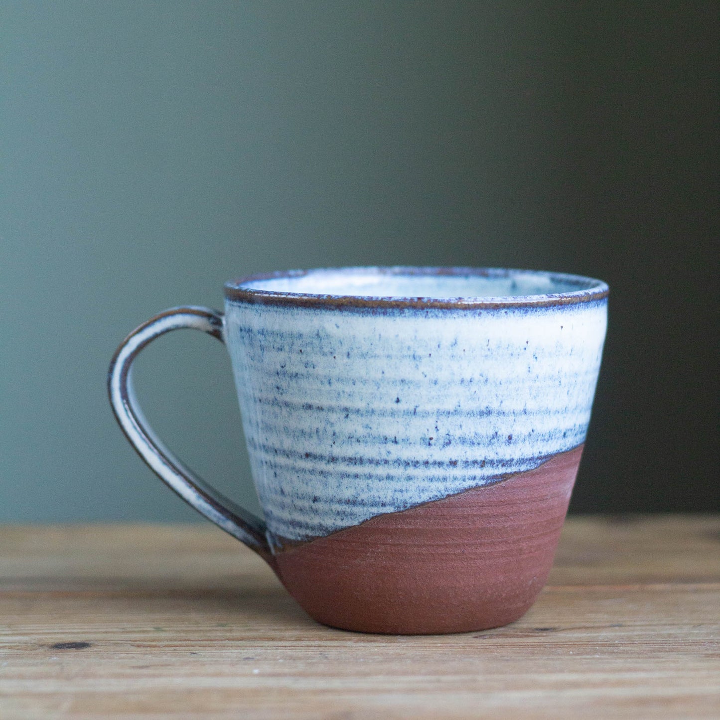 Ceramic mug with blue and red brown design on a wooden surface with a green background