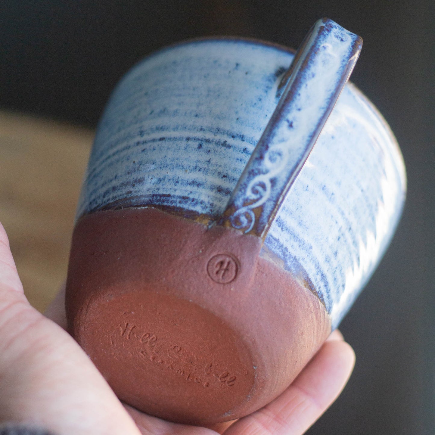 Hand holding a ceramic mug with blue interior and red brown exterior, blurred background