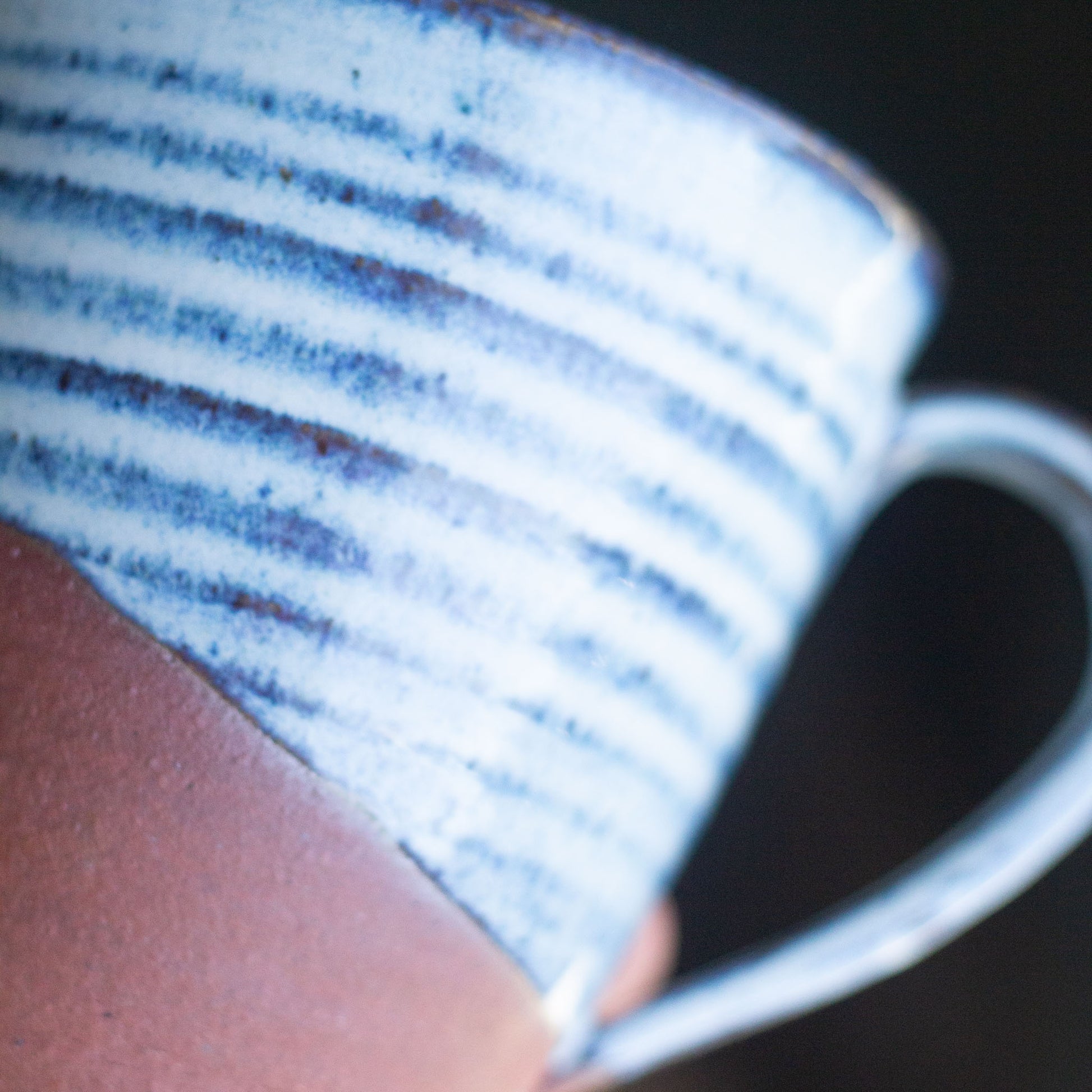 Close-up of a hand holding a blue and white ceramic mug with a dark background