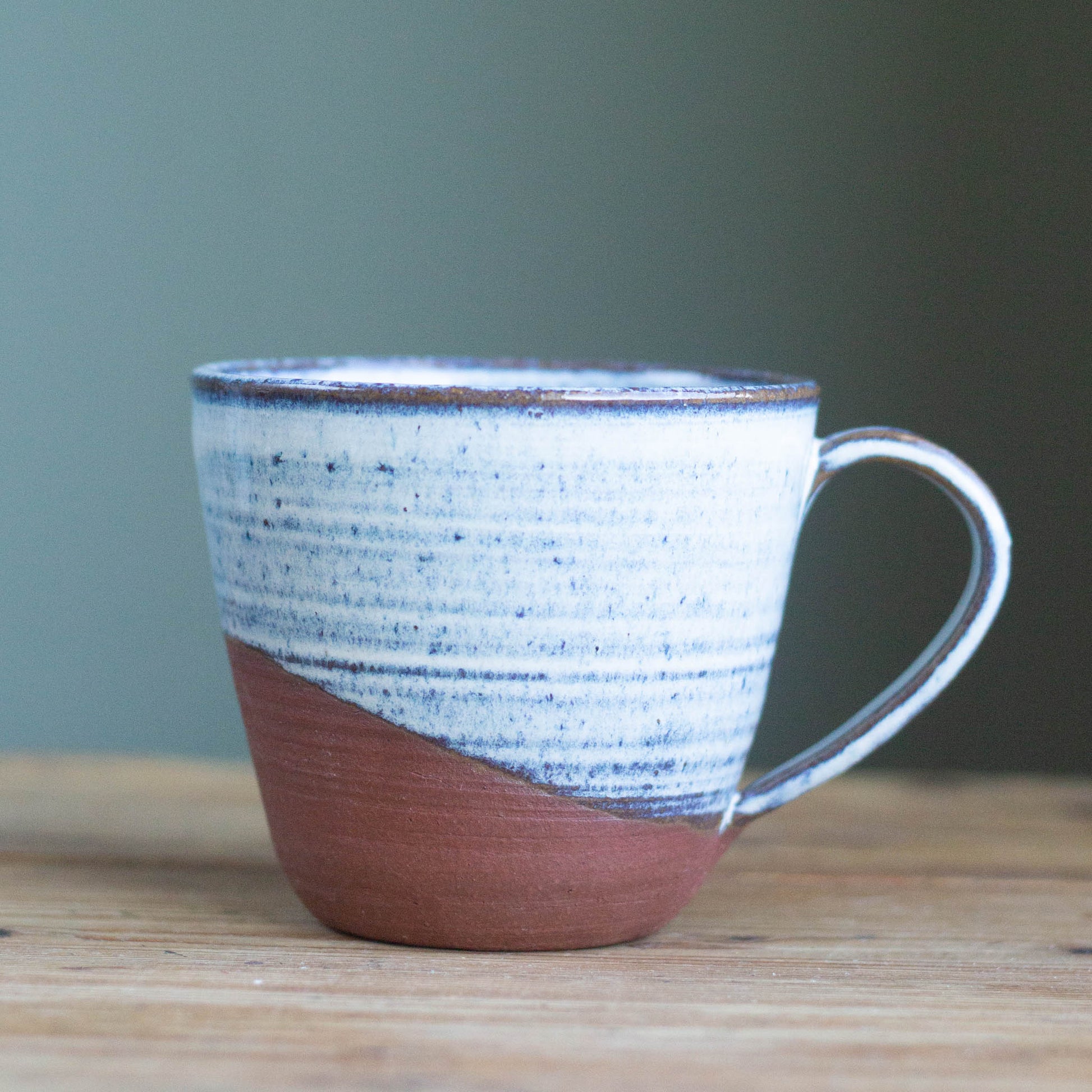 handmade ceramic tea mug with blue textred pattern and red clay on a wooden surface