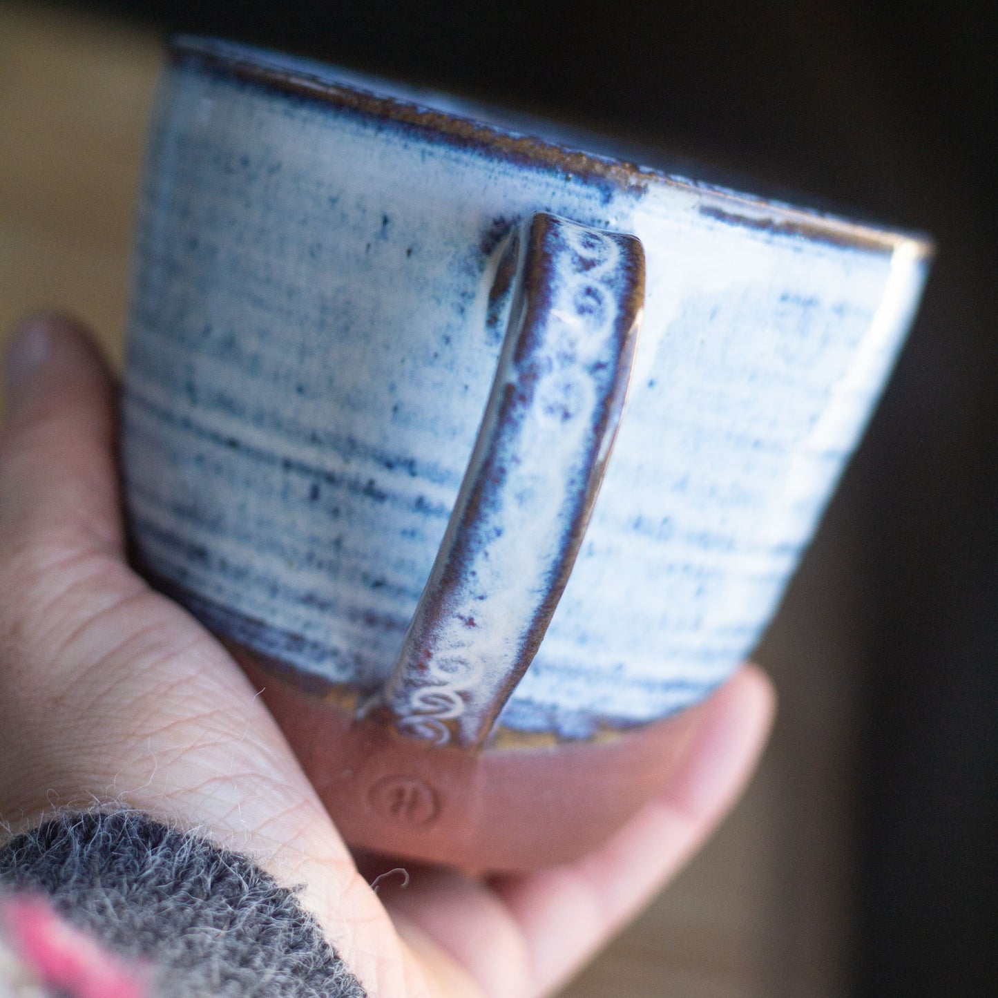 Hand holding a handmade blue ceramic cup with a textured surface