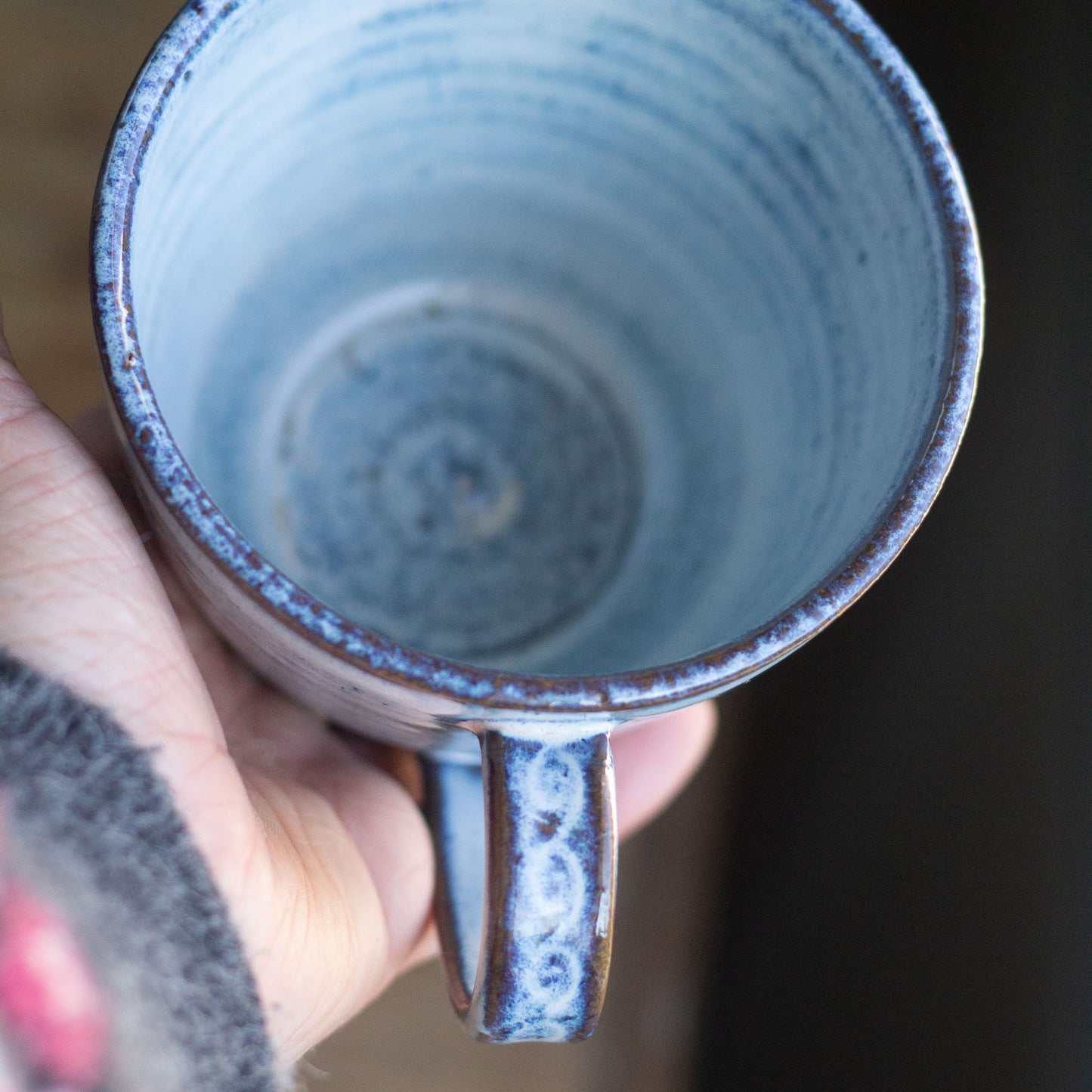 Hand holding a blue ceramic mug with a dark background