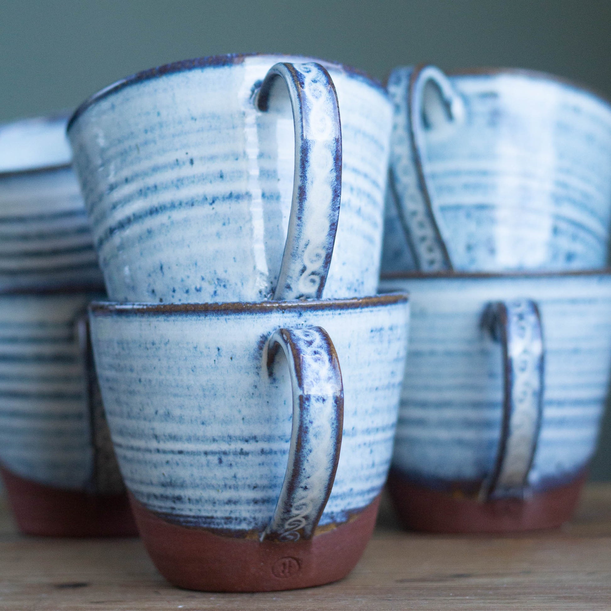 Set of blue and brown ceramic mugs with decorative handles on a wooden table