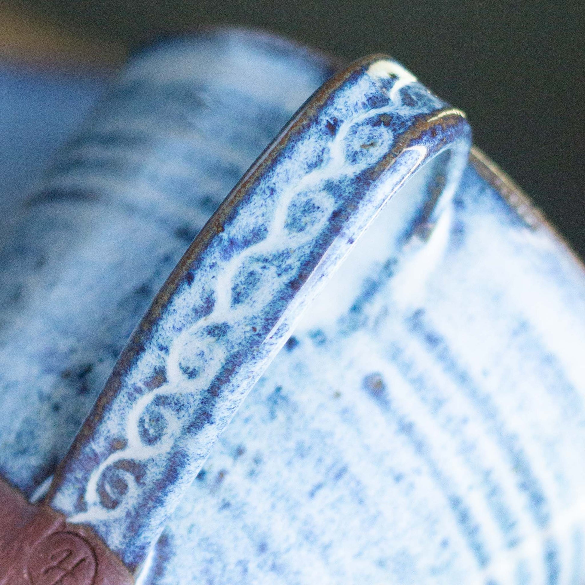 Close-up of a ceramic cup with blue glaze and intricate patterns on the handle