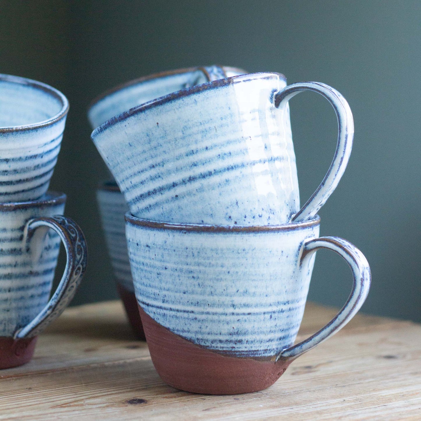 Set of ceramic tea mugs with blue and glaze on a wooden table.