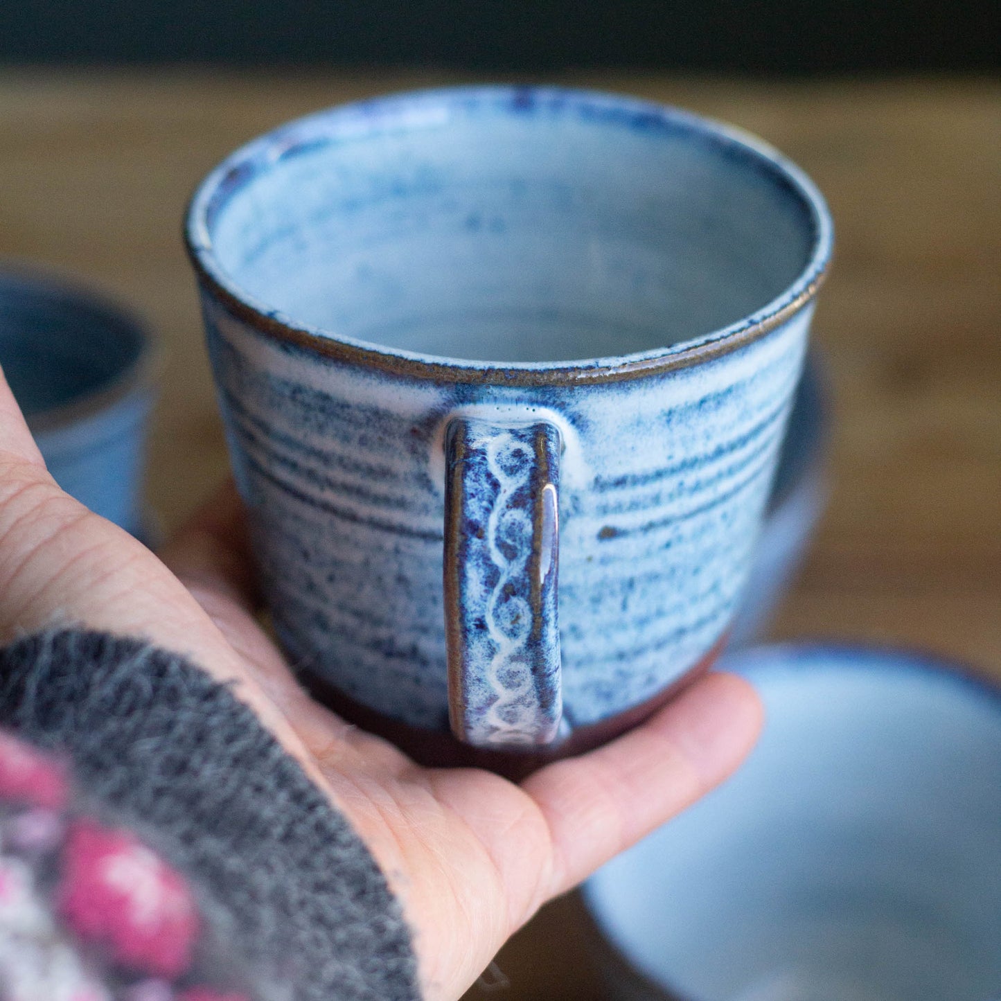 Hand holding a blue ceramic mug with a textured surface and decorative handle