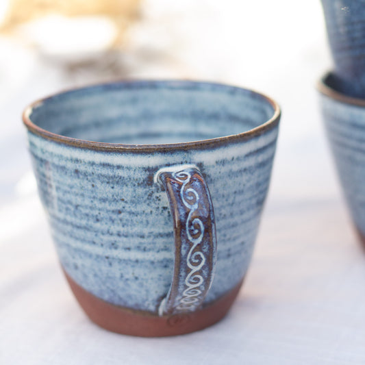 Blue handmade ceramic cup with decorative handle on a white surface
